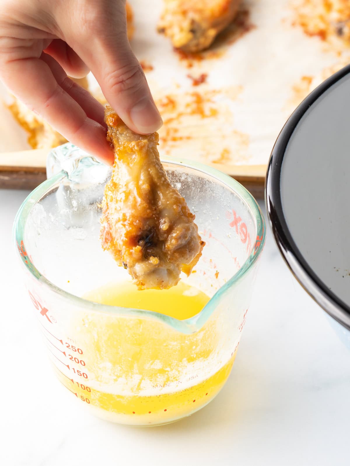 Hand dipping chicken wing into glass measuring container with melted butter.