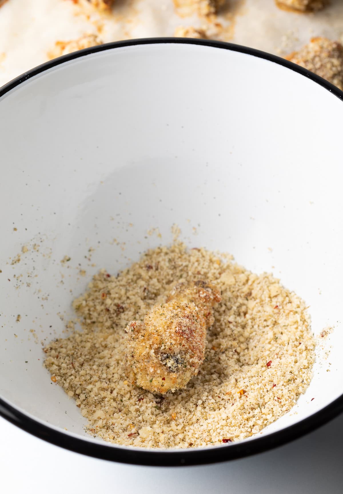 Tossing a wing in a white mixing bowl with breadcrumbs.