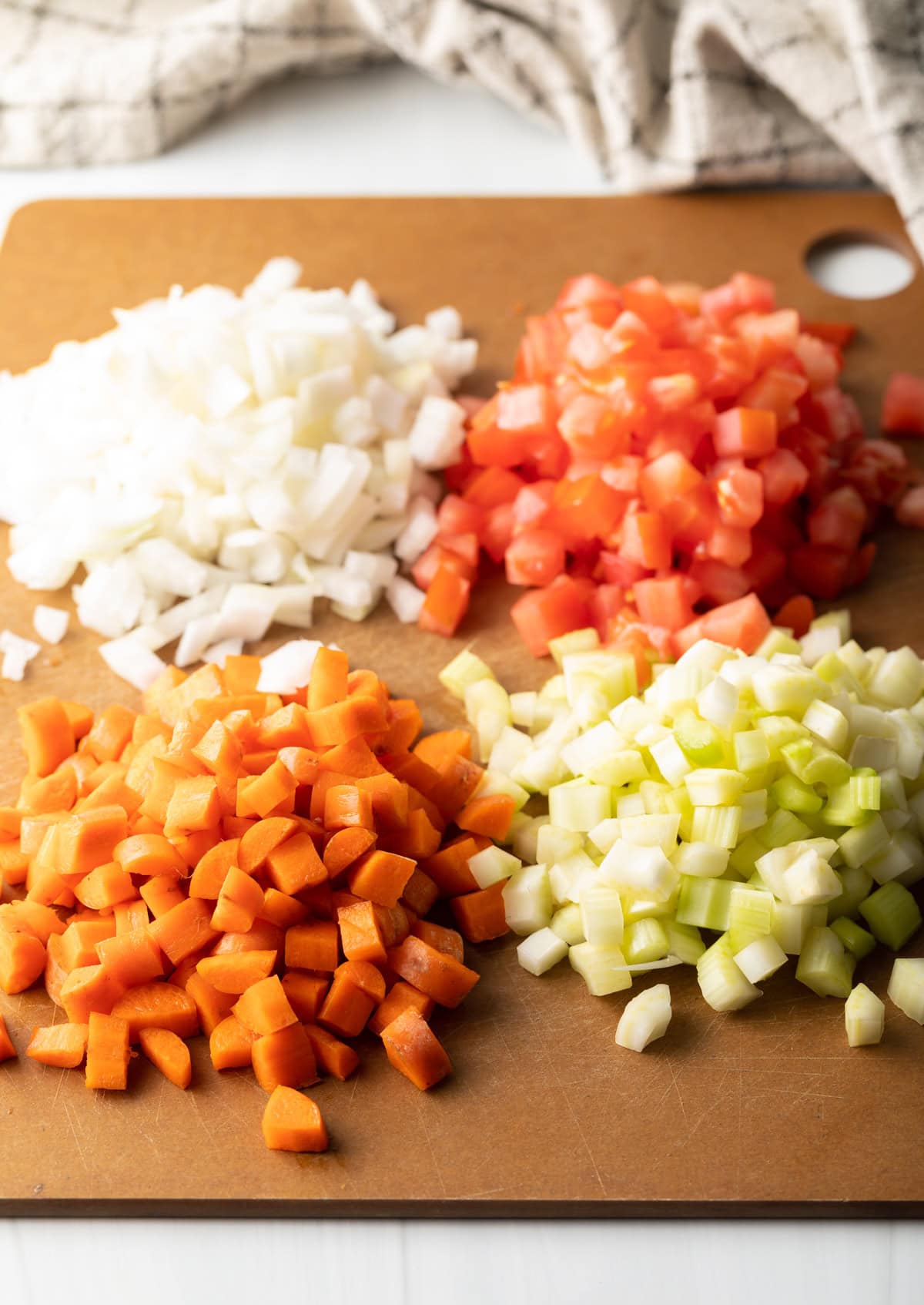 Mirepoux: diced tomatoes, white onion, celery, and carrots on a cutting board.