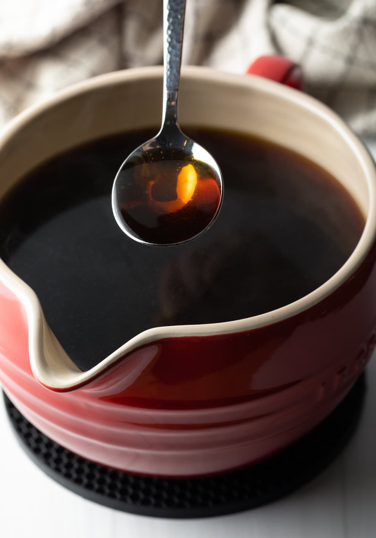 A spoon holding consomme over a ceramic bowl filled with consomme.