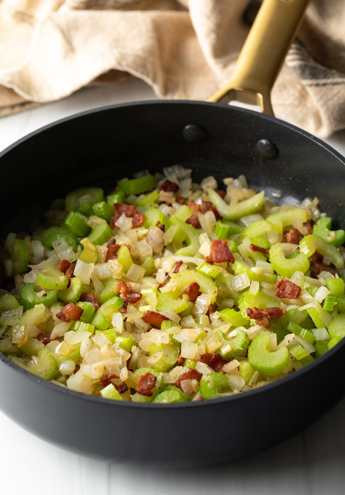 Sautéing diced bacon, celery and onions in a large black pan.