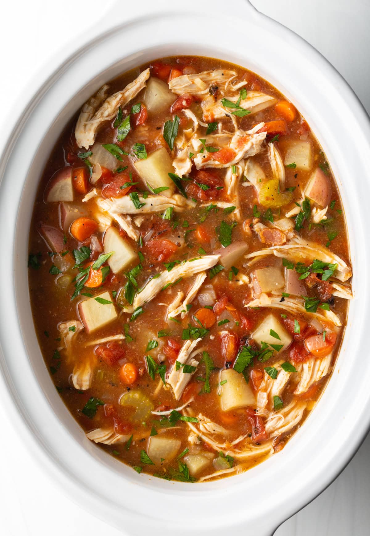 Healthy crock pot chicken stew in a white crock pot, ready for serving.