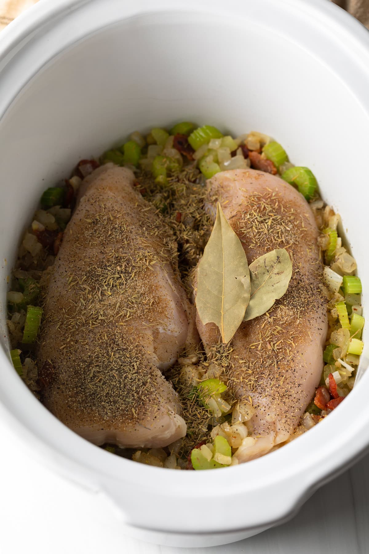 Two raw seasoned chicken breasts in a white crock pot.