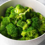 Bright green steamed broccoli in a white bowl.