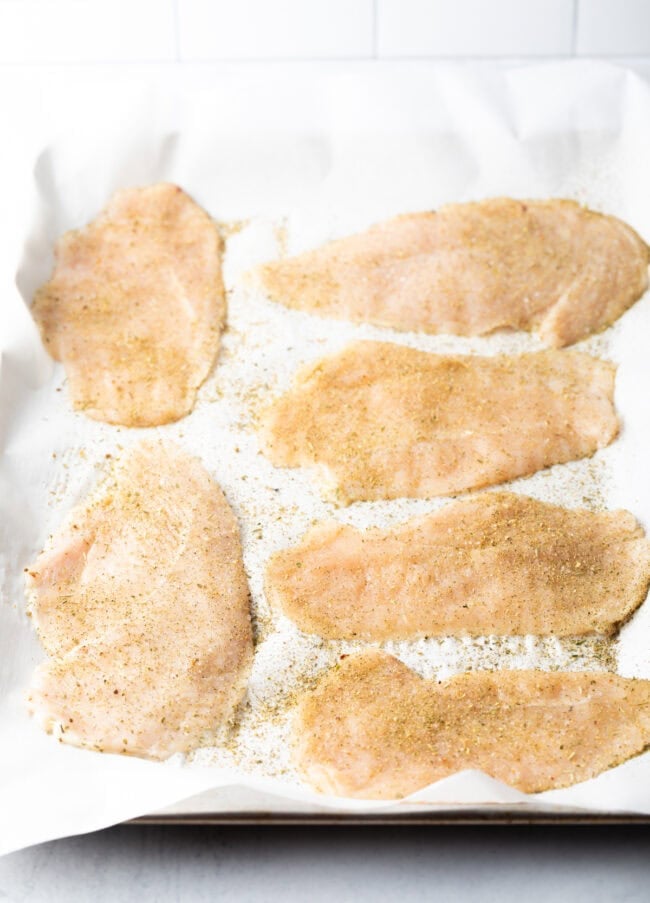 Chicken breast cutlets pounded thin on parchment, seasoned.