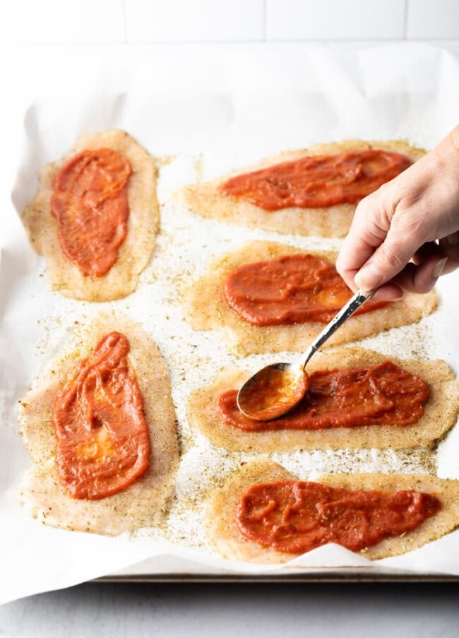 Hand with spoon adding tomato sauce to the cutlets.