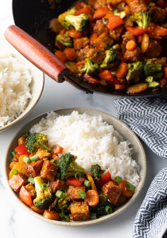 Top down view of plated vegan tempeh stir fry in a bowl with white rice.