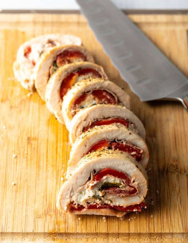 Stuffed chicken roulade, thin sliced on a cutting board with large knife.
