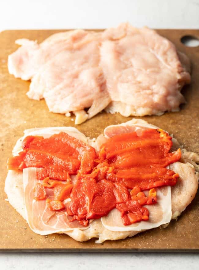 Slices of roasted red pepper laid flat on open slices of raw chicken. 