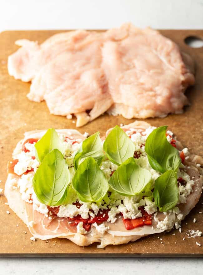 Butterflied chicken breasts split open, topped with prosciutto, red peppers, crumbled cheese and fresh baby basil leaves.