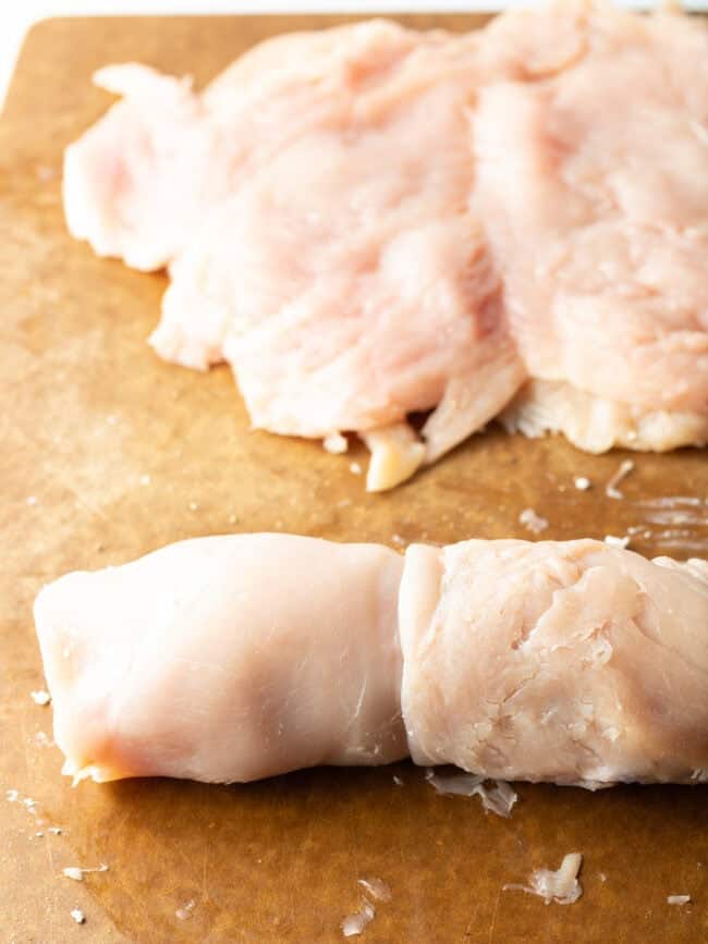Stuffed raw chicken rolled on a cutting board, wrapped with twine.
