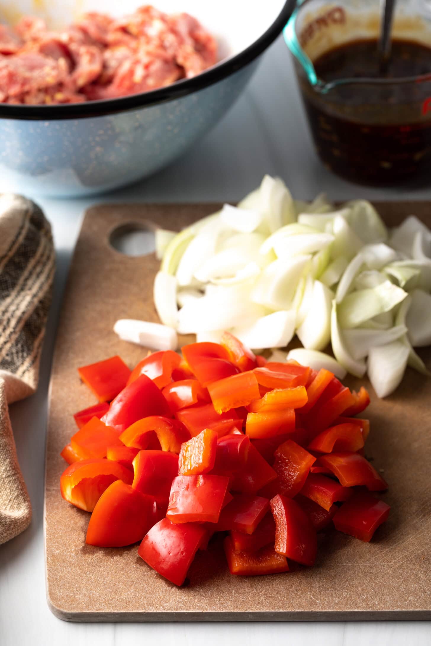 Chopped onion and red peppers on a cutting board.