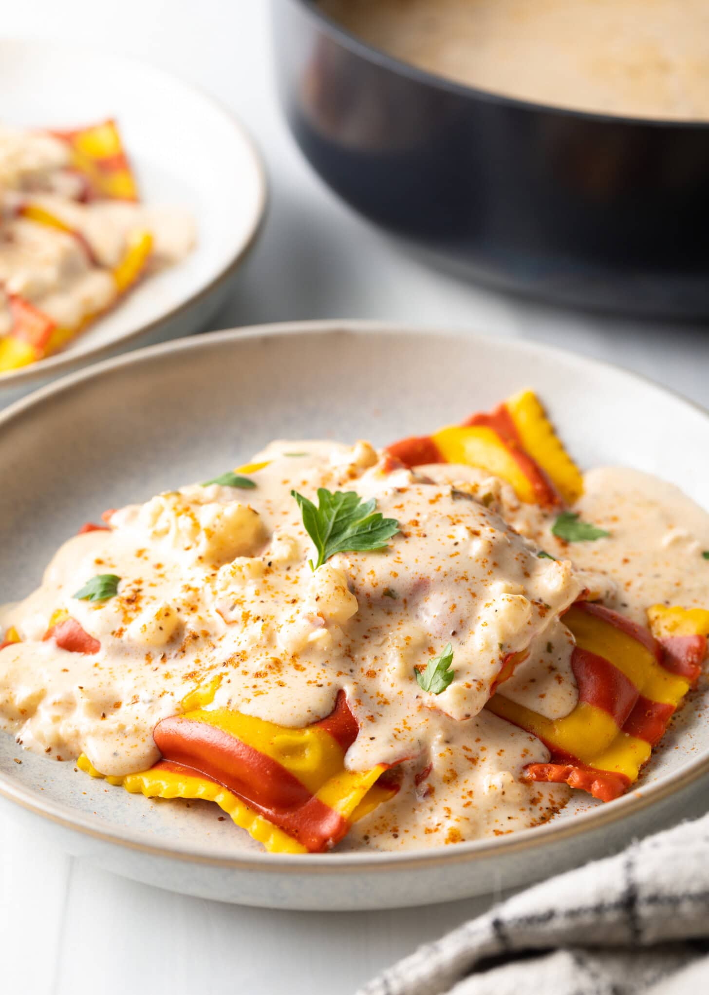 White plate with yellow and red striped lobster ravioli, covered in a rich Lobster Ravioli Sauce and sprinkled with parsley.