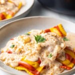 White plate with yellow and red striped lobster ravioli, covered in a rich cream sauce and sprinkled with parsley.