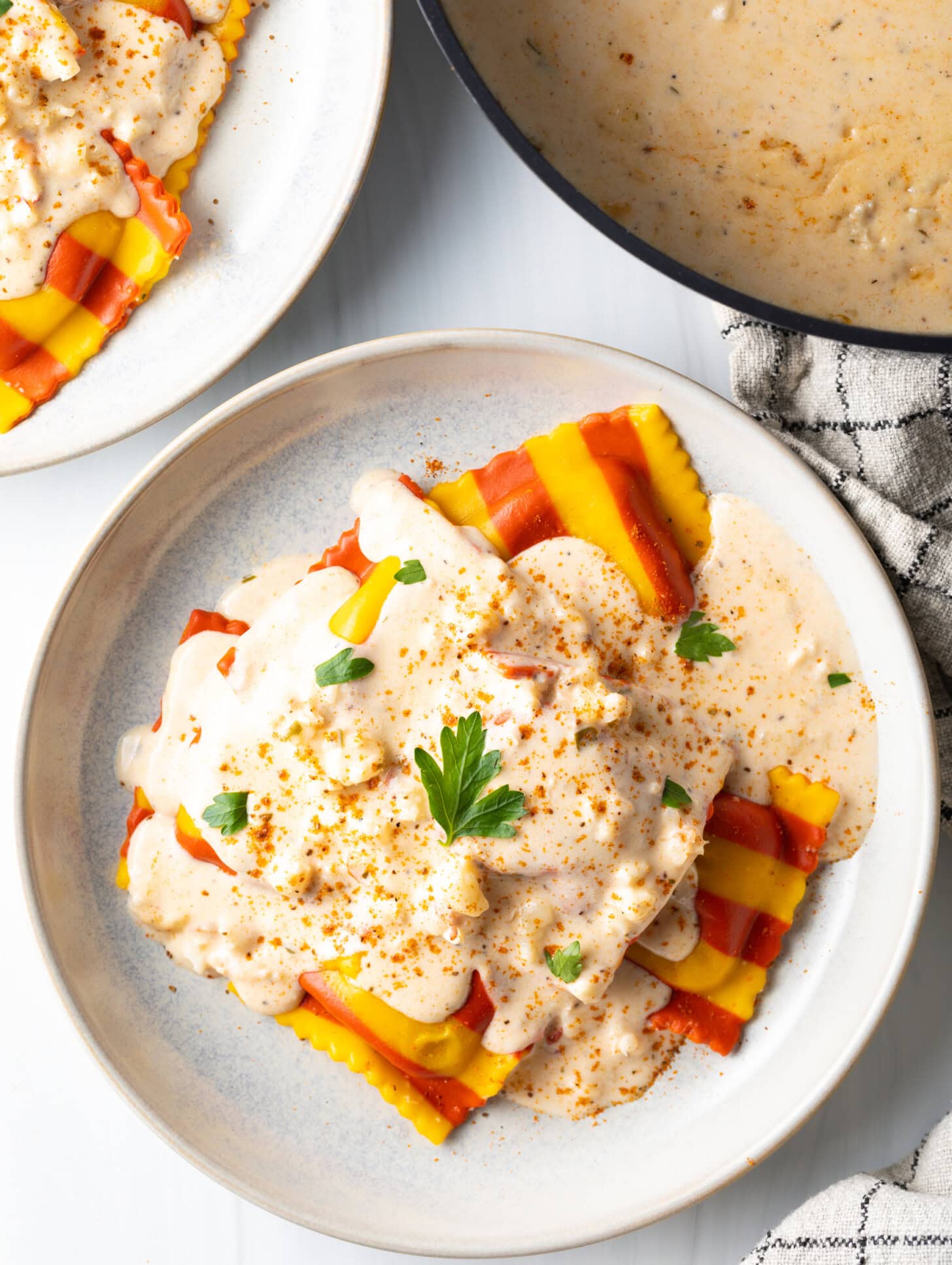 Top down view of a white plate with yellow and red striped ravioli, covered in creamy lobster sauce and sprinkled with parsley.