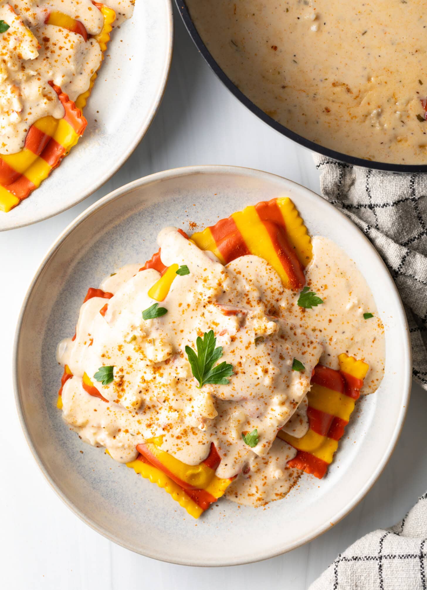Top down view of a white plate with yellow and red striped lobster ravioli, covered in a rich Lobster Ravioli Sauce.