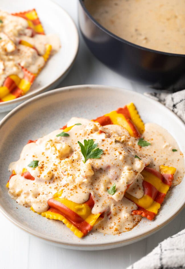 White plate with yellow and red striped lobster ravioli, covered in best sauce for lobster ravioli.