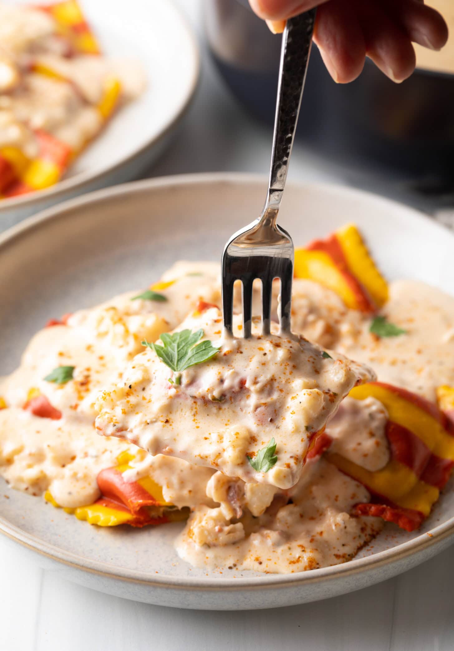 Fork cutting into ravioli on a white plate with creamy lobster sauce.