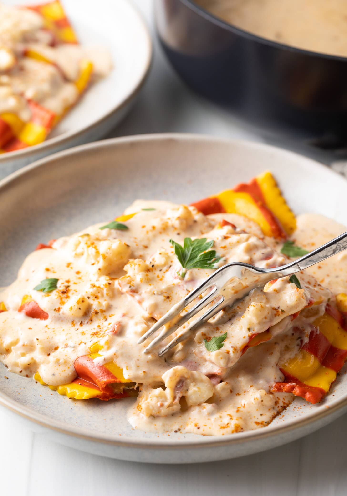 Fork cutting into ravioli on a white plate with the best sauce of lobster ravioli.