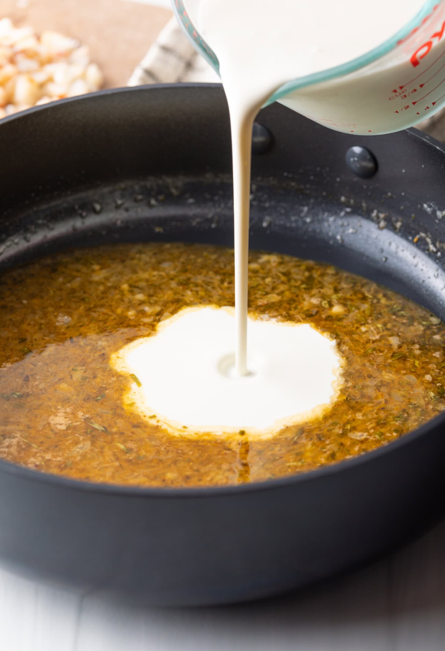Heavy cream poured into the pan with sherry and aromatics for Lobster Ravioli Sauce.