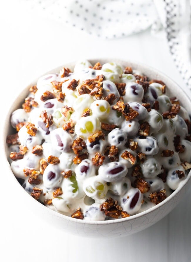Grape salad in a white bowl, topped with crunchy chopped pecans.