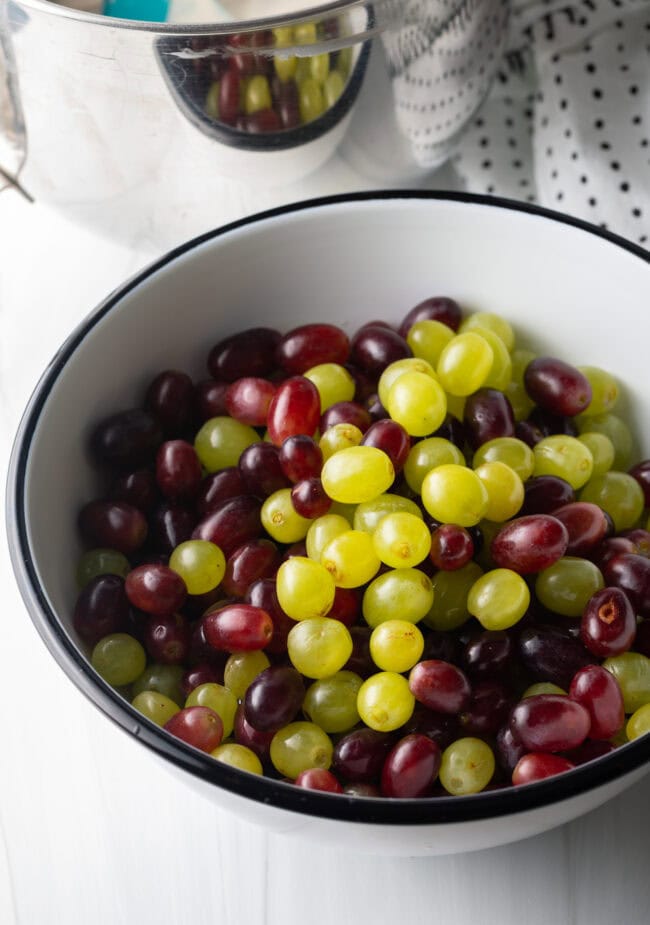 Green and red grapes, removed from the stems, in a white bowl.