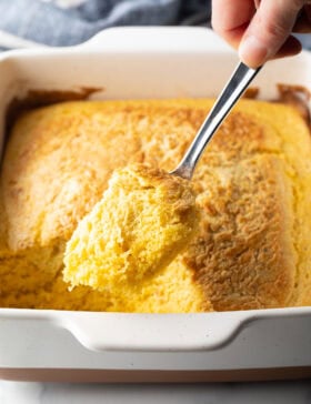 A top-down photo with a metal spoon showing a portion of a corn spoonbread dressing to the camera.