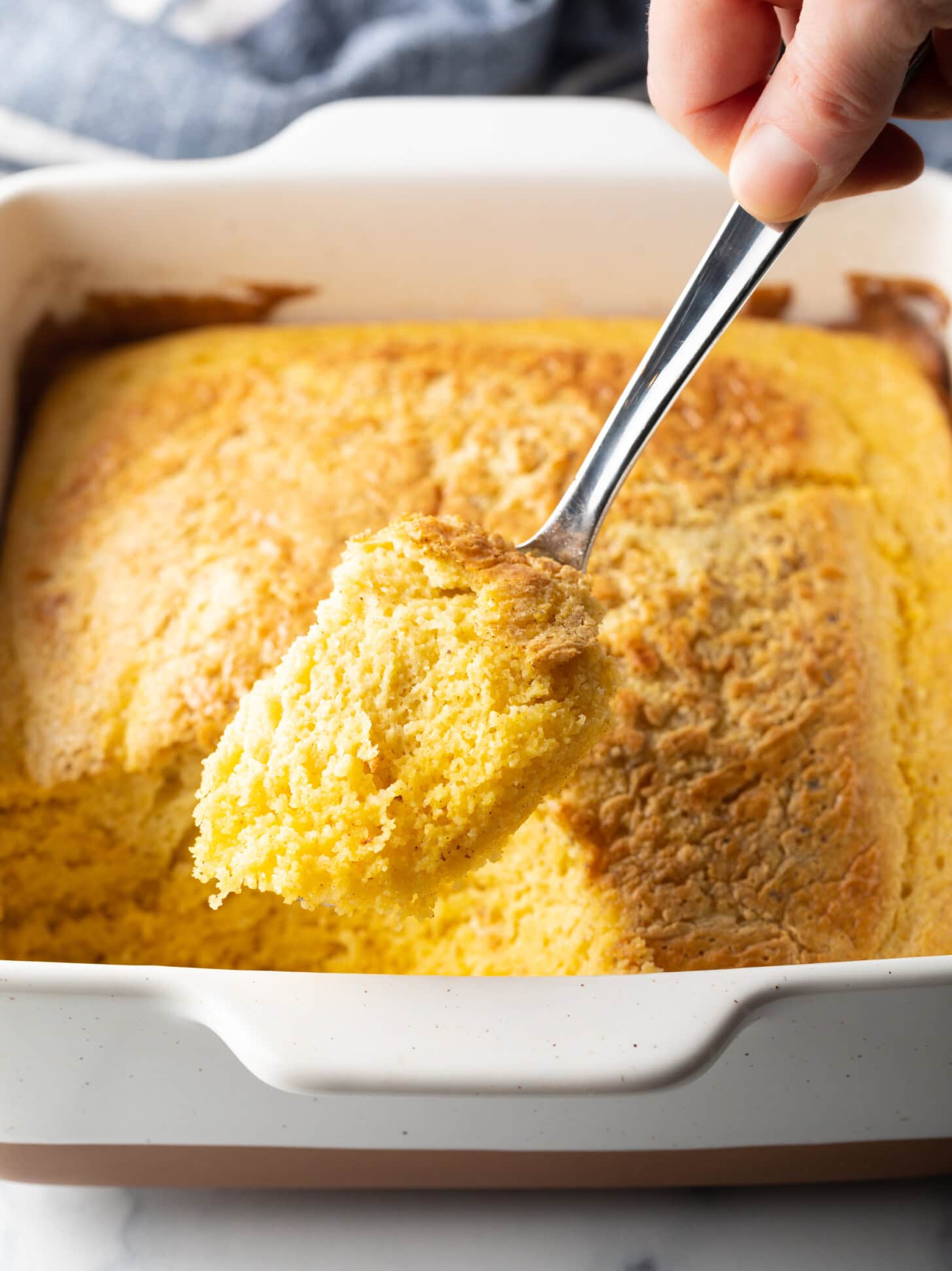 A top-down photo with a metal spoon showing a portion of a corn spoonbread dressing to the camera.