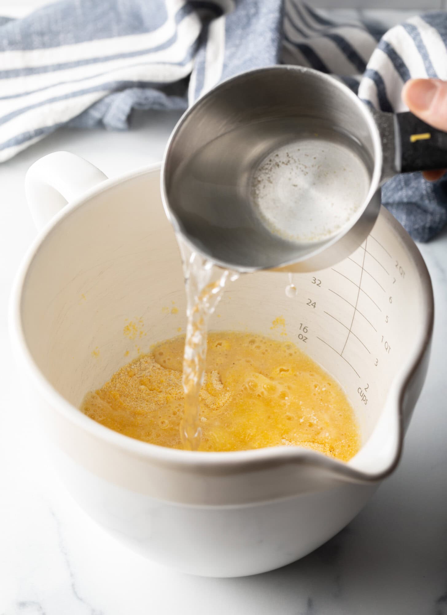 Adding water to the mixing bowl from a metal measuring cup.