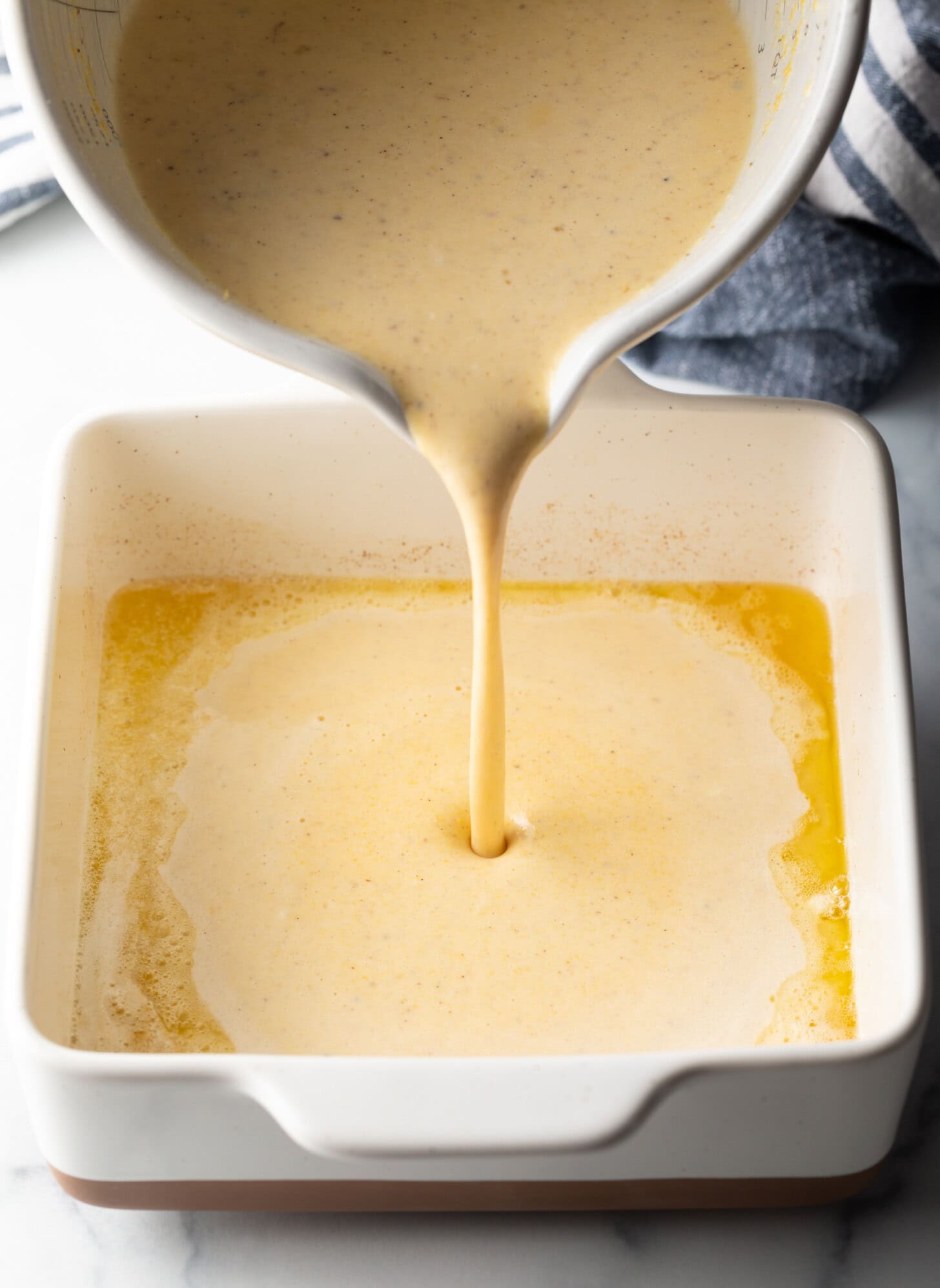 Pouring corn spoon bread mixture into a white baking dish.