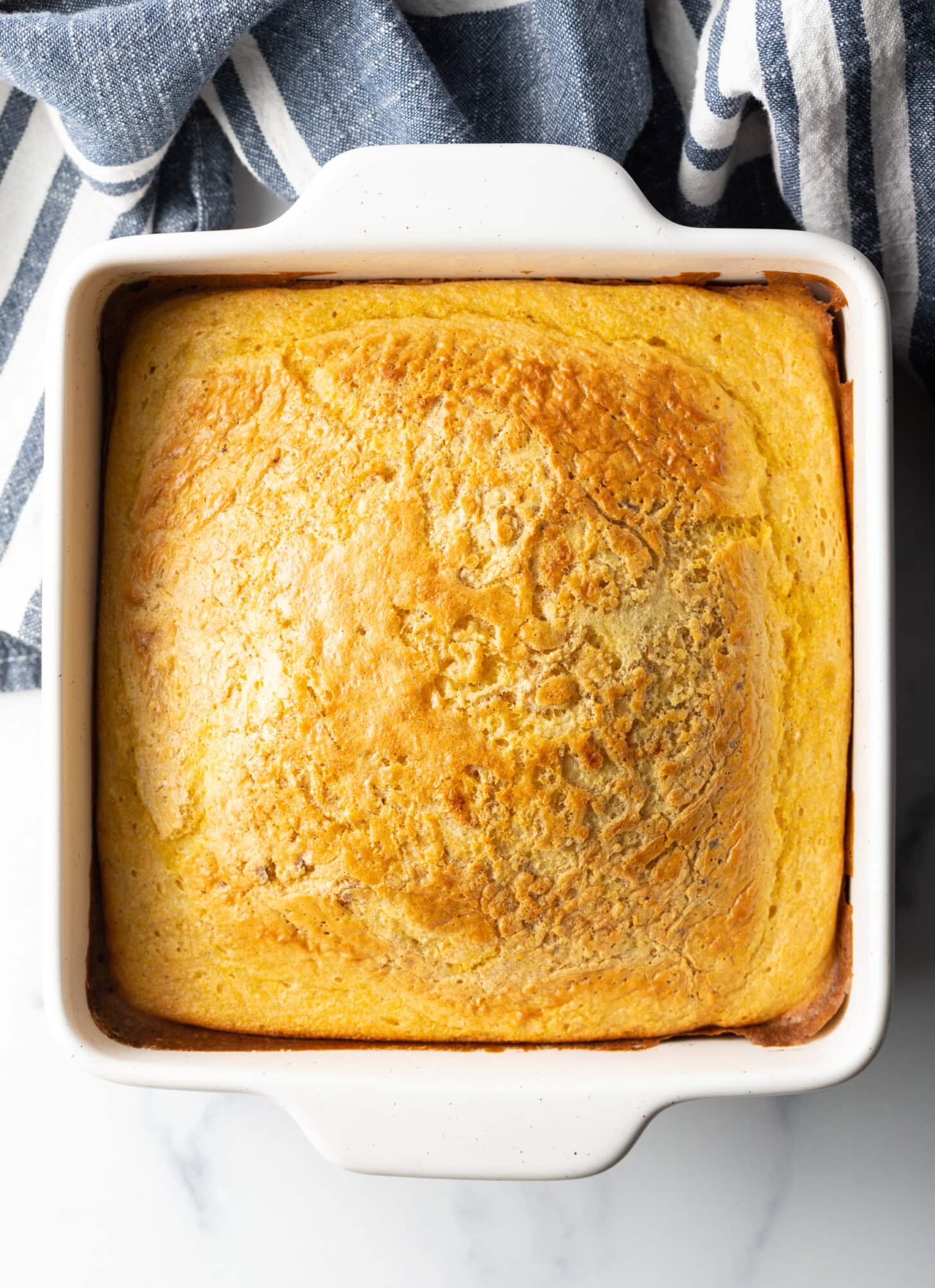A top-down shot of baked corn spoon bread in a white square dish.