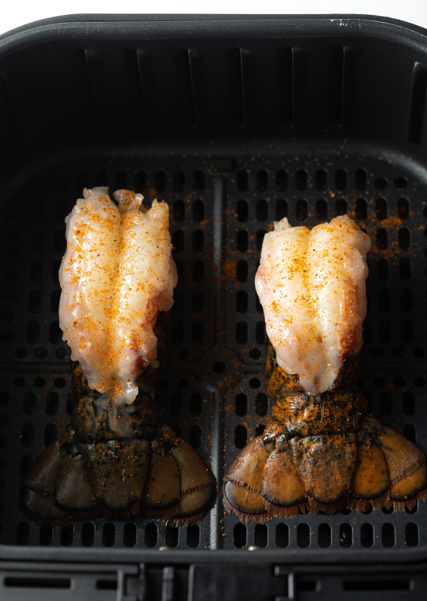 Two raw lobster tails in an air fryer.