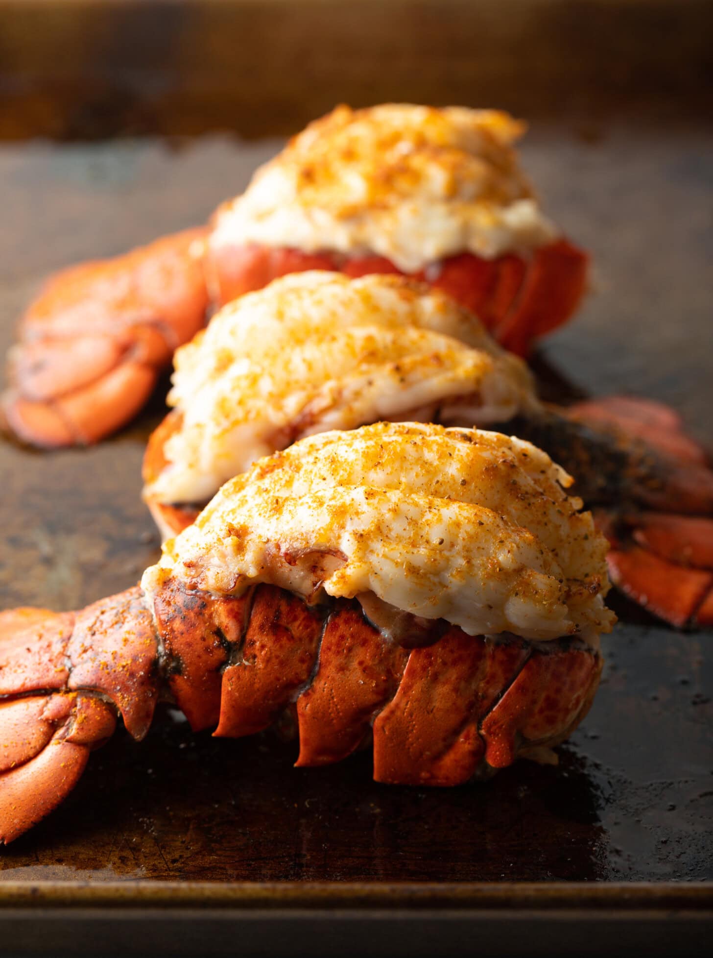 Three plump cooked lobster tails on a baking sheet.