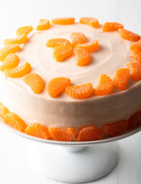 Round cake with white frosting and ring of mandarin slices around the top and bottom of the cake.