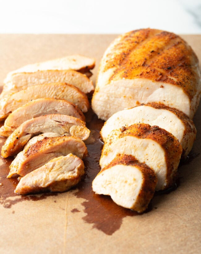 Close view of a smoked chicken breast and a chicken thigh on cutting board. Chicken breast is sliced into 4 large pieces. Thigh is sliced into 7 pieces.