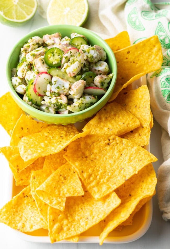 Green bowl of aguachile verde. Bowl is surrounded by yellow corn tortilla chips.