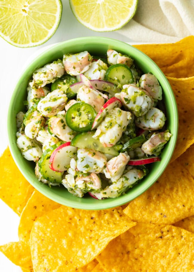 Green bowl of aguachile verde. Bowl is surrounded by yellow corn tortilla chips.