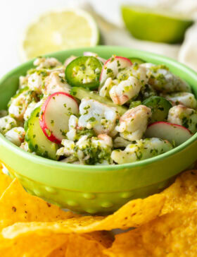 Green bowl of aguachile verde. Bowl is surrounded by yellow corn tortilla chips.