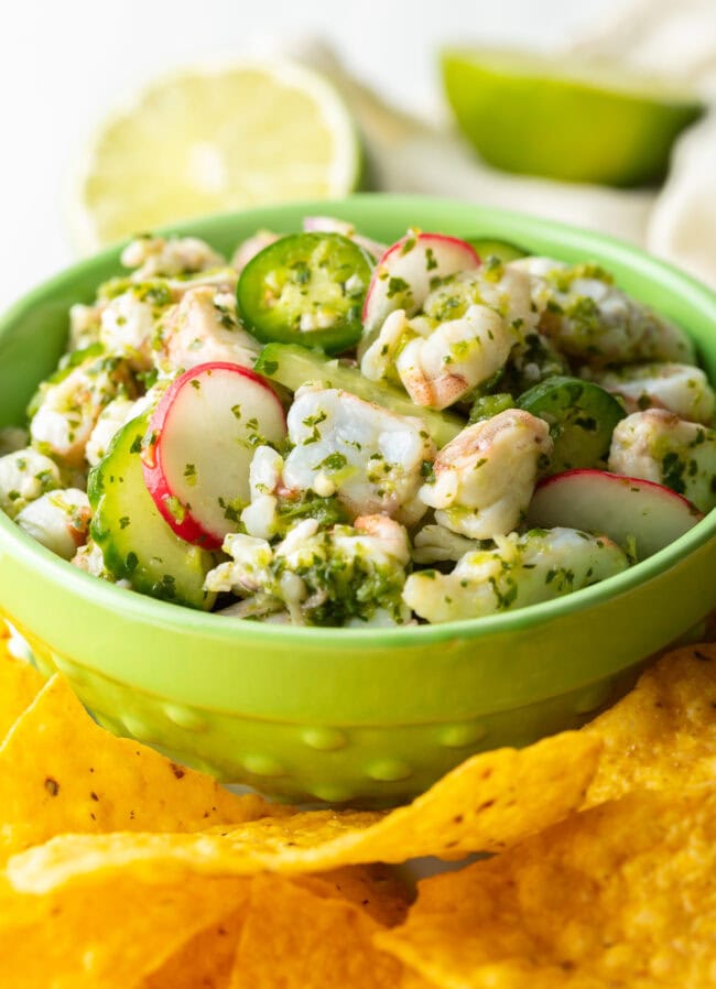 Green bowl of aguachile verde. Bowl is surrounded by yellow corn tortilla chips.