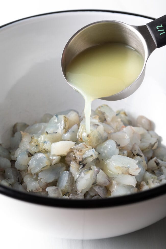 Adding lime juice to chopped shrimp in a white bowl.