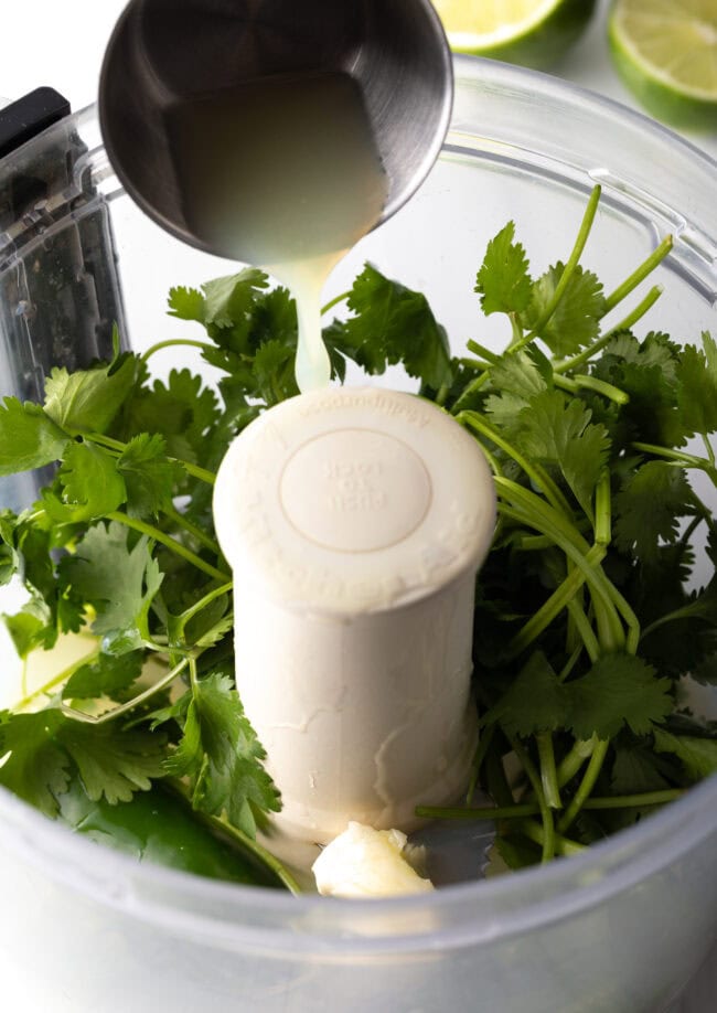 Adding lime juice to the food processor with cilantro.