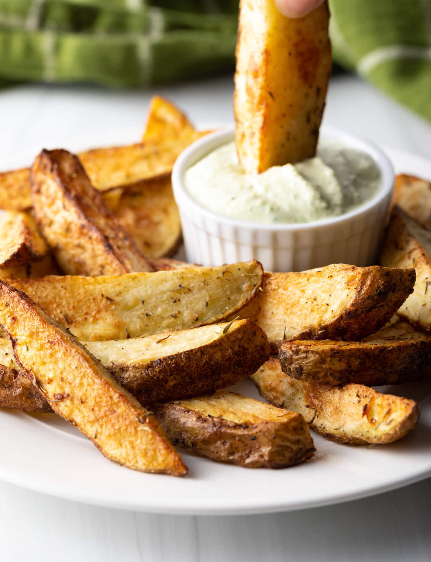 A hand dipping a crispy air fryer potato wedge into a ramekin of white sauce.