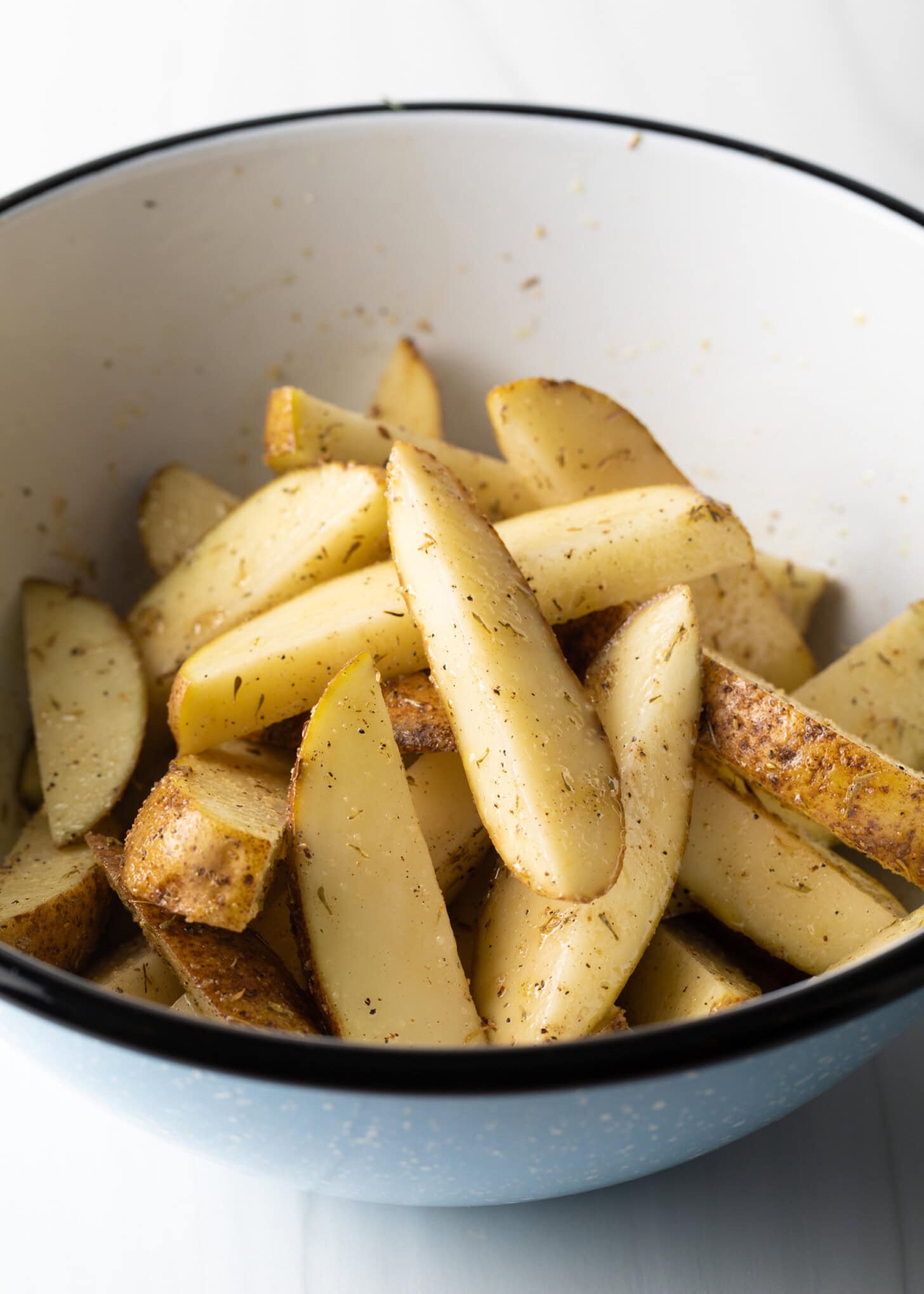 Thick sliced sections of potato in a white bowl, tossed with oil and seasonings.