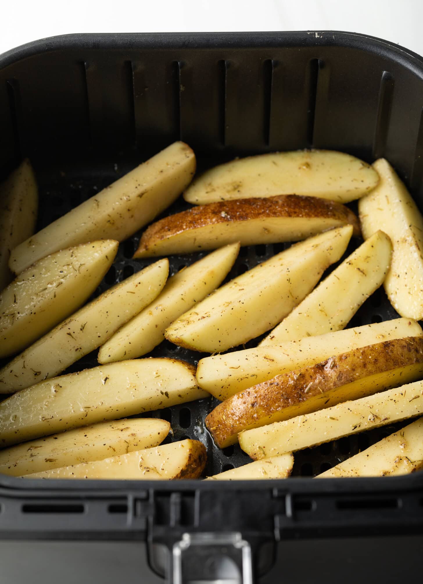 Raw potatoes in thick slices, evenly spread in the air fryer basket.