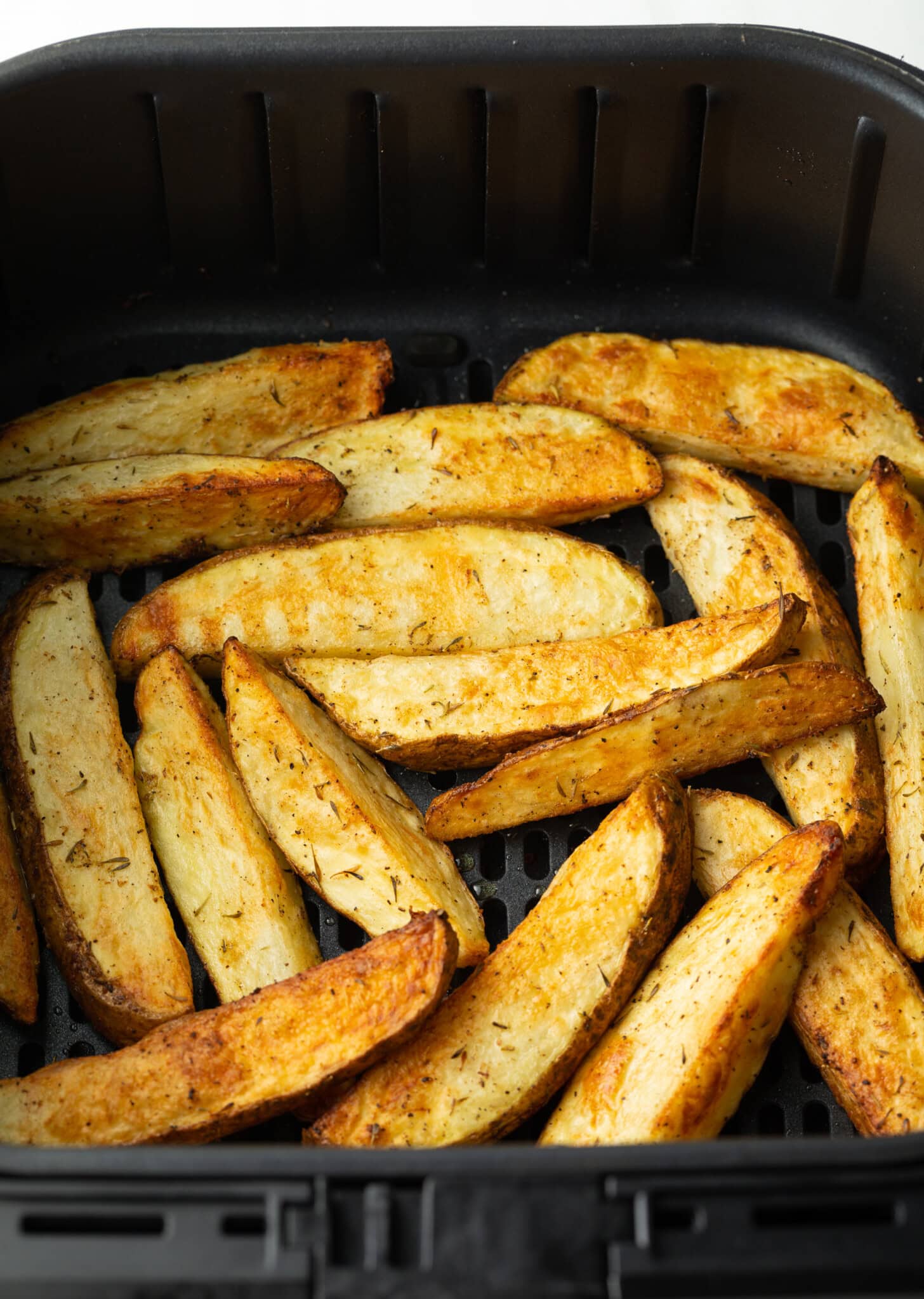 Crispy air-fried potato wedges in a black air fryer basket.