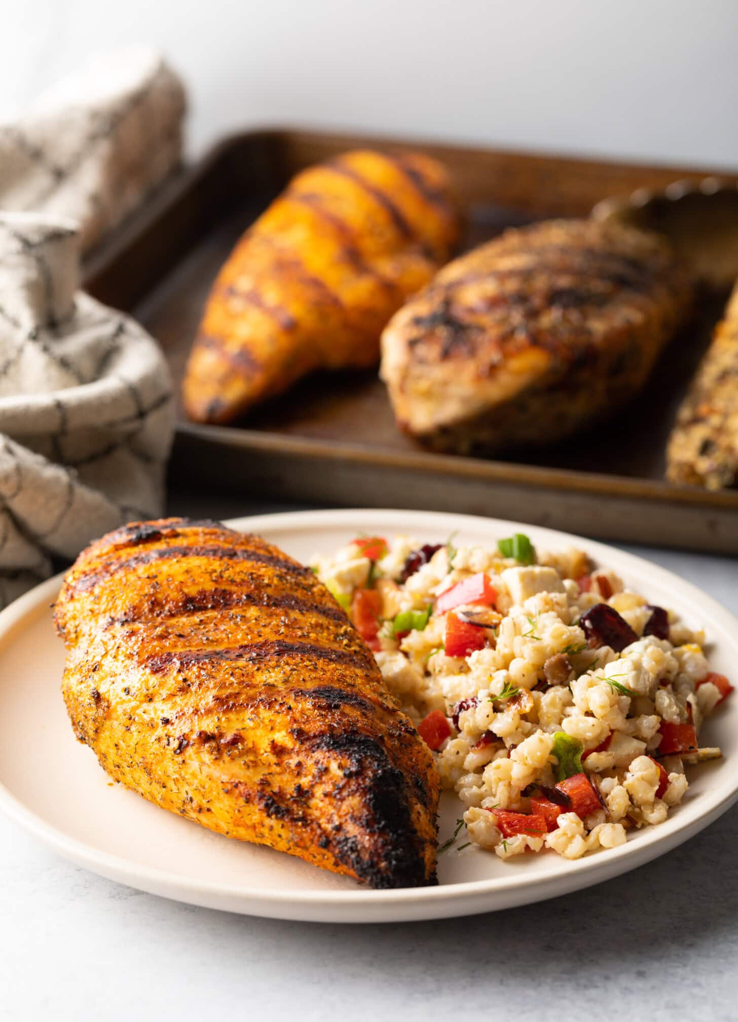 One whole chicken breast seasoned and grilled, resting on a white plate next two a side of bean salad.