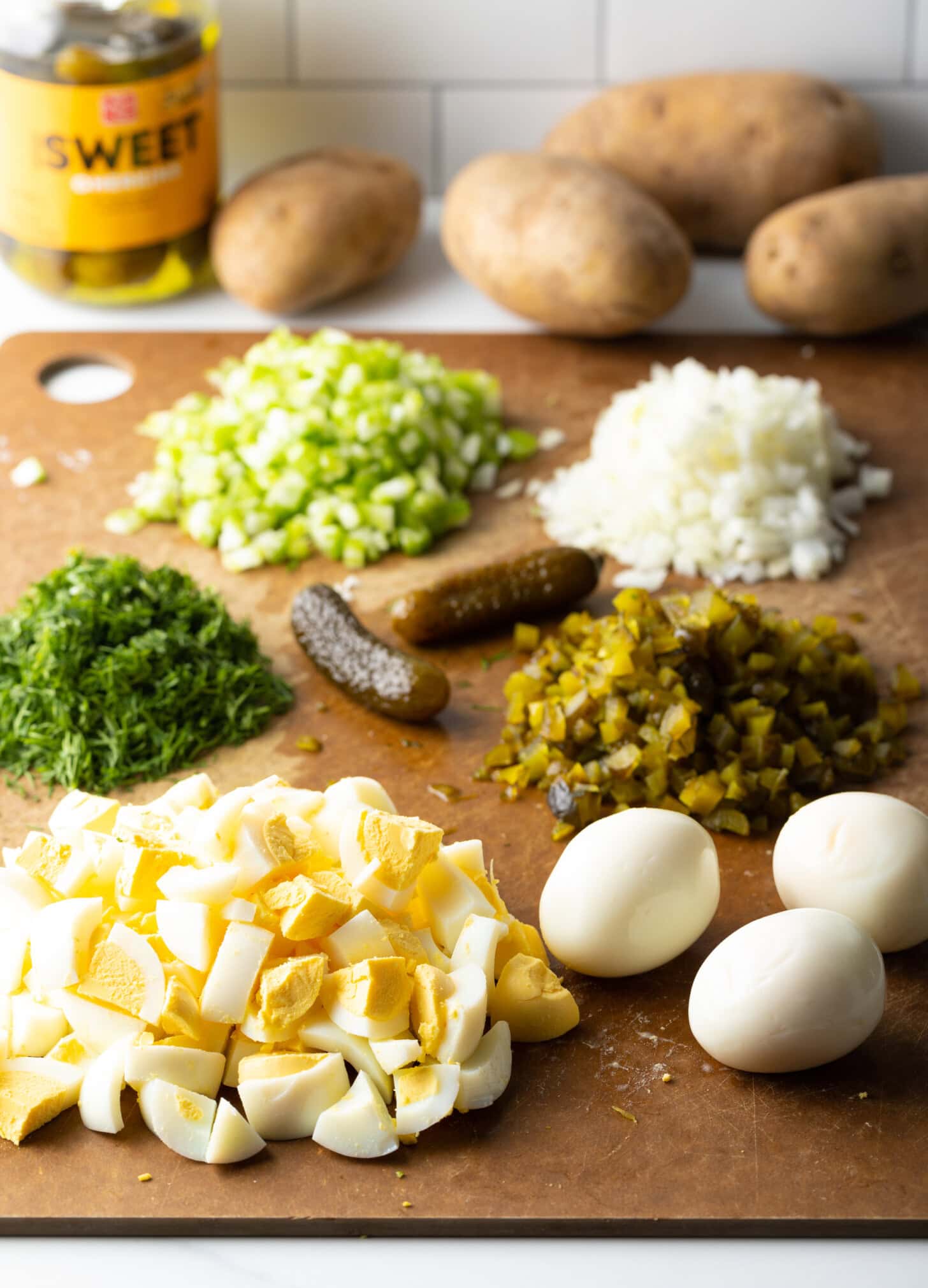Prepared and chopped ingredients for making deviled egg potato salad on a cutting board.