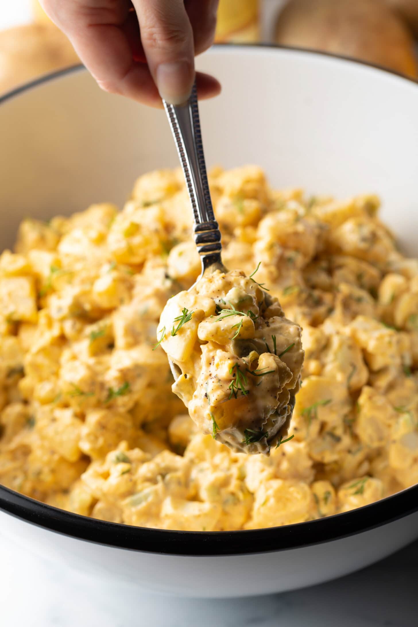 Metal spoon showing a bite of deviled egg potato salad to camera.
