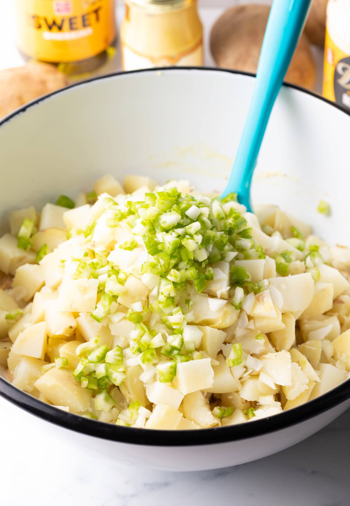 Chopped celery on top of a bowl of not yet mixed potato salad.