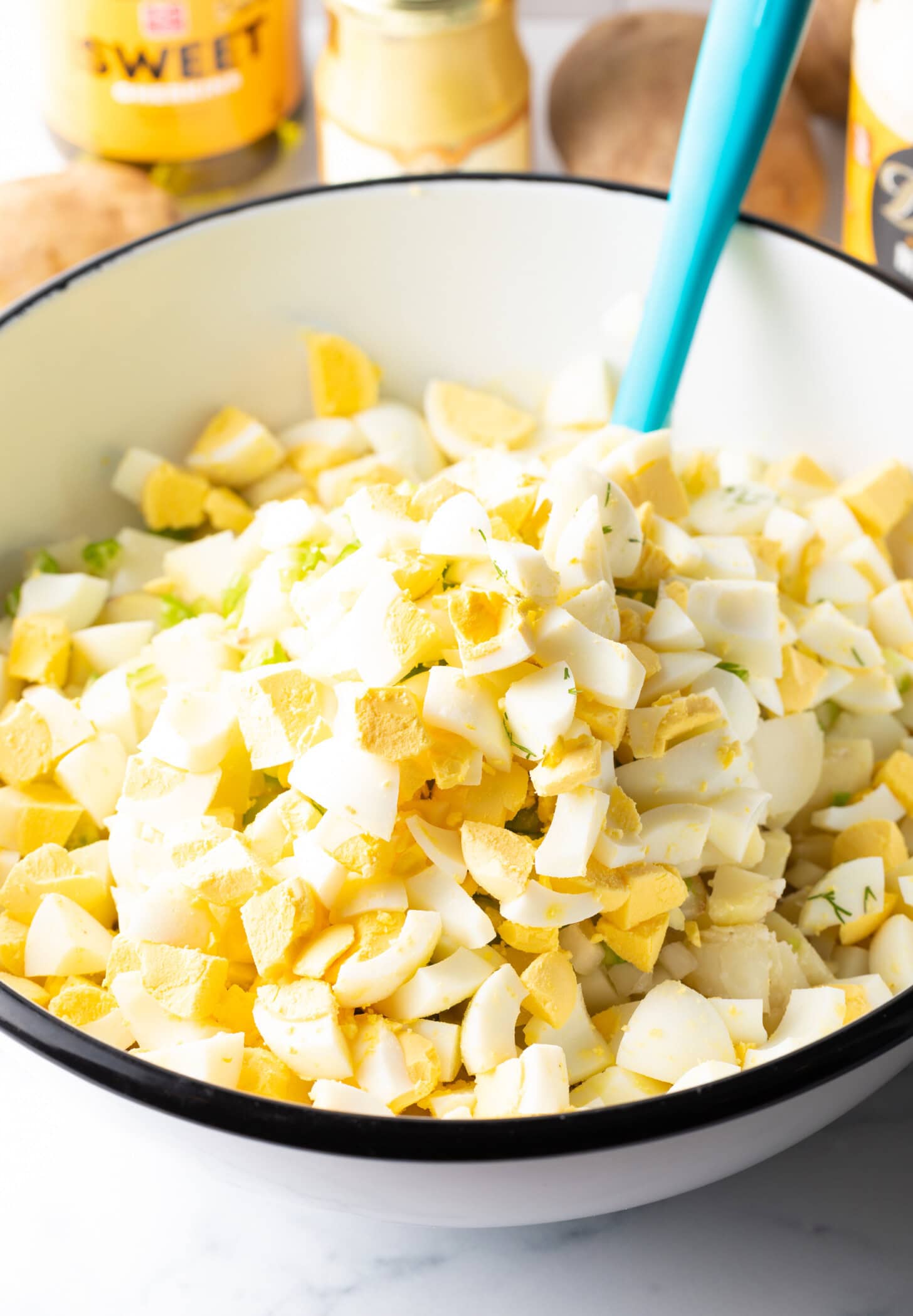 Chopped eggs on top of a bowl of potato salad just before it is stirred together.